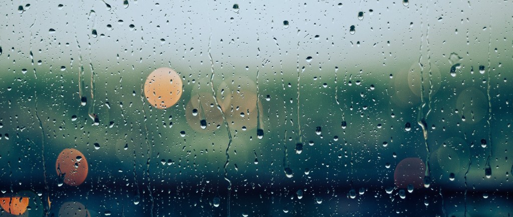 Poetry rain drops on a glass with a blurred background of green and lights