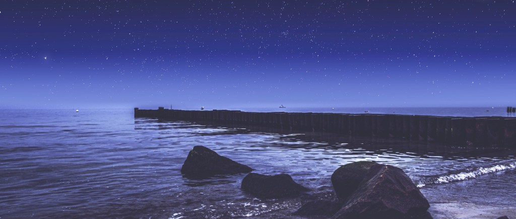 poem starry night with shores of the sea, a few rocks jutting out and a pier to the sea